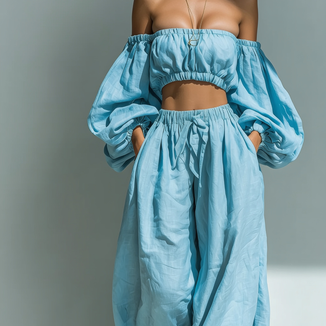Model in light blue off-the-shoulder top and wide-legged pants against a gray background.